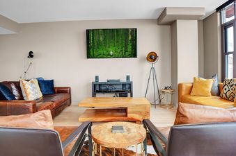 A cozy living room at The Lowell 301B with leather sofas, a modern coffee table, and a wall-mounted TV displaying a forest scene.
