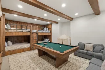A spacious games room with a pool table, built-in wooden bunk beds, a gray sofa, and a patterned area rug.