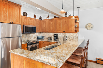 A fully equipped kitchen at Top of the Village Leaf 401, featuring stainless steel appliances, granite countertops, and a breakfast bar with seating.