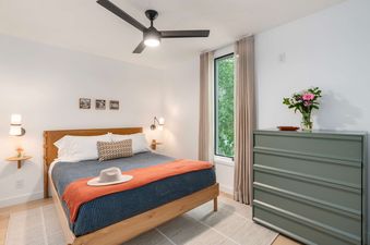 A modern, bright bedroom at Cottonwood Jackson Hole with a wooden queen-size bed, sage green dresser, and a window viewing green trees.