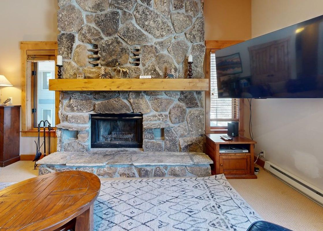 Cozy living area in Rendezvous D3 featuring a grand stone fireplace and a large flat-screen TV.
