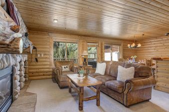 A living room with a large leather sofa, a fireplace, and a large window looking out to a forest.