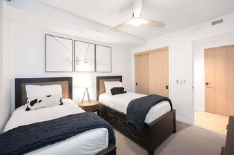 A modern twin bedroom at Electric Pass Lodge 308 featuring two beds with dark wood frames, white bedding, navy blue knit throws, and a cow print accent pillow, complemented by ski lift art and a light wood closet.