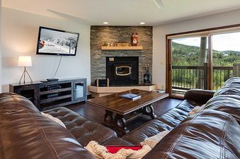 The living room of Ranch at Steamboat RA309 features brown leather couches, a fireplace, and a flat-screen TV, with a view of mountains from the balcony.