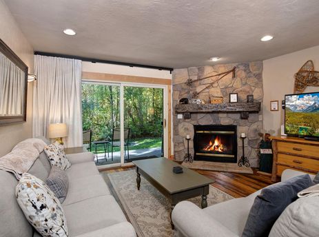 A cozy living room featuring a stone fireplace with a warm fire, a television displaying a mountain scene, and a comfortable sofa.