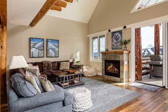 The living area of Saddle Ridge Townhome Unit J1, showcasing a cozy fireplace, comfortable seating, and rustic wooden beams.