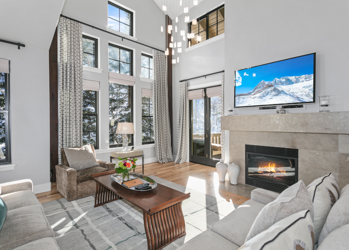 The living room of the Lodges at Deer Valley 2 Bedroom Suite features a large flat-screen TV above a fireplace, two large comfortable couches with plush pillows, and a coffee table with a vase of flowers.