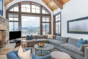 A living room with a large sectional sofa, a fireplace, and a stunning view of the mountains through a large arched window.