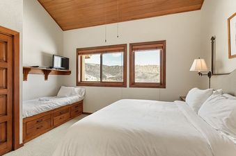 A cozy bedroom in Woodrun V Residence 5 features a queen bed, a daybed with a wall-mounted TV, and two large windows offering mountain views.
