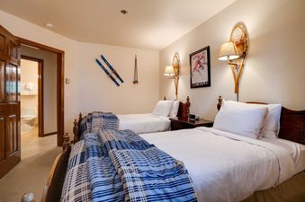 A cozy bedroom at Chateau Chamonix CX233 with two twin beds, ski-themed decor, and an inviting entrance to a bathroom.