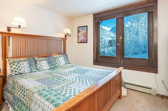Manitou Lodge 1 Hotel Room Bronze Rated showcases a cozy bedroom with a wooden bed frame, a colorful quilt, and a window view of a snowy landscape.