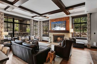 A spacious and elegantly furnished living room in Flagstaff 208, featuring dark leather furniture, a fireplace, and a large TV, with views of the outdoors through expansive windows.
