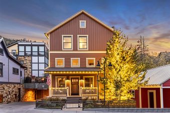 The Peak at Town Lift is a warm and inviting multi-story brown home adorned with festive string lights and a beautifully lit Christmas tree, all set against a stunning twilight sky.