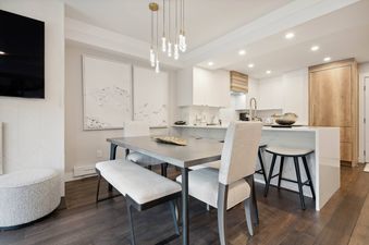 The dining area of Lodge Tower 278 2BR features a modern metal dining table and a bench, as well as two chairs, with a view of the kitchen, a marble countertop, and a wooden cupboard.