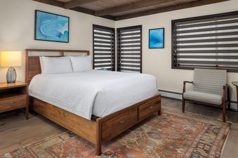 A serene king bedroom in Willows C3 with a wooden bed frame, white bedding, a nightstand with a lamp, and blue abstract art on the walls.