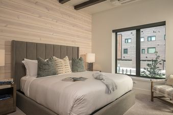 A modern and cozy bedroom at Princetown Grande with a large bed, upholstered headboard, and a window offering an urban view.