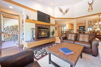 A cozy living room at The Charter D4505 with a fireplace, TV, and leather sofas, with a view of the kitchen and a stack of firewood.