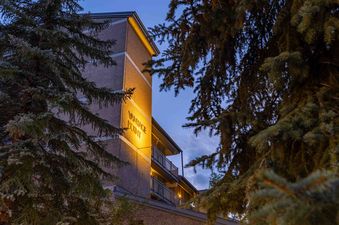 A low-angle exterior shot of the Vantage Point 501 at twilight, with the building's illuminated sign framed by dark pine trees and a clear blue sky.