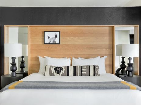Modern King bedroom with a wooden headboard, decorative throw pillows, and unique bedside lamps at Gravity Haus JH King.