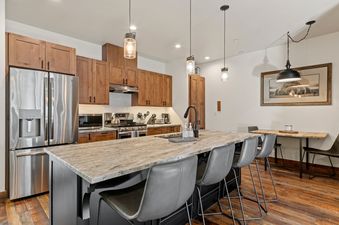 A modern kitchen with wooden cabinets, stainless steel appliances, a large granite island with seating, and hardwood floors in Baker Loft 201.