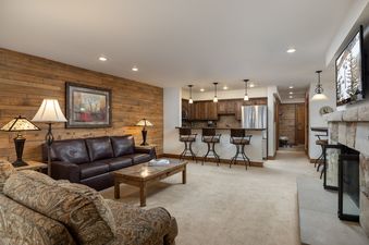 The Montaneros 321 living area features a comfortable brown leather sofa, a wood coffee table, and a stone fireplace.