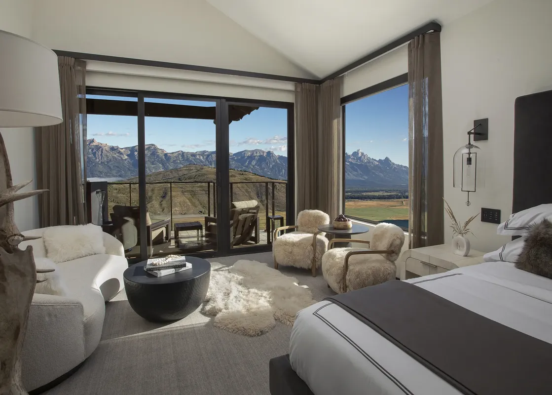 A luxurious bedroom and lounge area in The Grand Teton Suite, featuring a bed, plush seating, and expansive windows offering breathtaking mountain views.