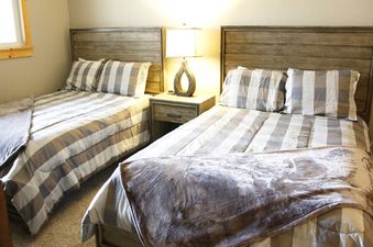 Two neatly made beds with striped comforters and throw blankets are in a bedroom at Meadow Ridge 8 Unit 6, with a nightstand and lamp between them.