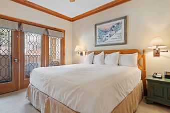 A master bedroom in The Charter D2505 with a large bed, wooden headboard, white bedding, and double French doors leading to a balcony.