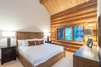 A rustic bedroom in Tristant 125 features a comfortable bed, bedside tables with lamps, and a window offering a view of the natural surroundings.