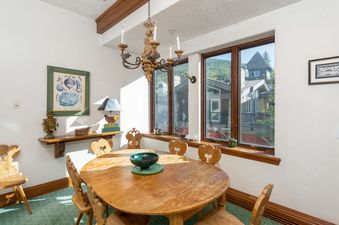 A rustic dining area at Plaza Lodge 2 Bedroom Silver Unit 3, featuring a wooden table and chairs, a chandelier, and large windows with an exterior view.