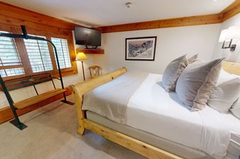 The bedroom in Manor Vail 242 has a comfortable king-size bed with a wooden headboard, fluffy pillows, and a cozy throw blanket.  The bedroom has a view of the trees outside.
