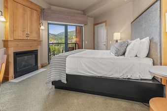 A Steamboat Grand Deluxe King bedroom with a fireplace, a king-sized bed, and a balcony view of mountains.