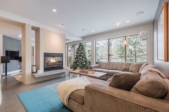 Modern living area with a fireplace, comfortable sectional sofa, and floor-to-ceiling windows showing a snowy landscape.