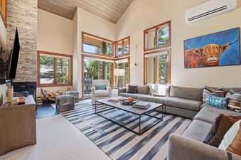 Modern and bright living room in Ridgepoint Townhome 166 with a large sectional, stone fireplace, and high ceilings.