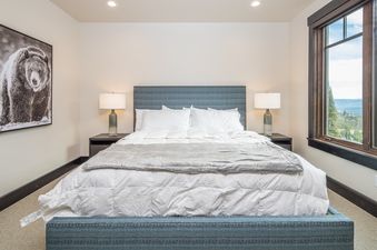 A cozy bedroom at 7 Lower Cascade Ridge features a bed with white linens, a blue textured headboard, modern lamps, and a window with a mountain view.