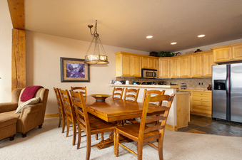 A cozy dining area featuring a wooden table and chairs, illuminated by an elegant chandelier, with an adjacent fully equipped kitchen at Antlers at Lakota 406.