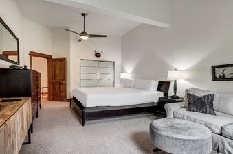 The primary bedroom features a king-sized bed, a ceiling fan, and a comfortable sofa area, all set against a backdrop of light-colored walls and carpet.