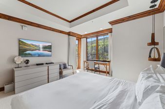 A luxury bedroom at the Alpine at the Ritz Carlton featuring a king bed, work desk, and a scenic view of the surrounding forest.