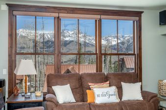 A cozy living area in Trails Edge 8 featuring a plush brown sofa and a large window looking out onto snow-capped mountains.