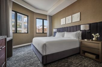 The king bed is central to the room, with crisp white sheets and a plush headboard, offering a luxurious feel. The room is beautifully appointed, with a desk in the corner, a side table, and a contemporary style.