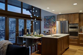 A modern dining area in Landmark 704 with a set table and an adjacent kitchen, featuring large windows overlooking a snowy mountain landscape.