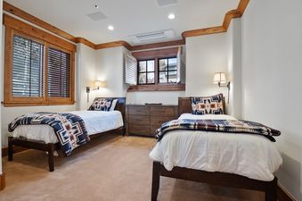 A cozy secondary bedroom at Timber Lodge at the Oaks features two twin beds with patterned blankets, a wooden dresser, and warm wooden accents around the windows and ceiling.