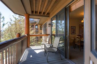 Private balcony with outdoor seating at Christie Club 316, featuring wooden decking and railings, with a view of green trees and the resort area.