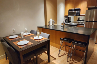 The dining area and kitchen of Aspens on Blackcomb Unit 113 are presented, highlighting a set table for four and a modern kitchen space.
