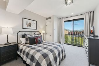 The bedroom at The Mason 3026 features a queen bed with buffalo plaid bedding, a nightstand with a lamp, and a sliding glass door leading to a balcony with mountain views.
