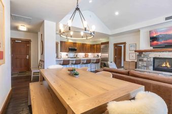 A modern, open-concept living space with a large dining table, a kitchen counter, a fireplace, and a flat-screen television.