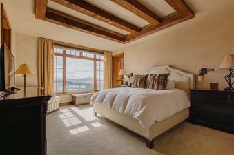 A luxurious bedroom featuring a large bed with white bedding, plush pillows, and an expansive window offering mountain views.