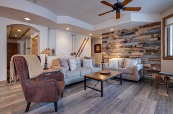 The living area of Chateau Chamonix CX326 features a brown leather armchair, two sofas with decorative pillows, a wooden coffee table, and a unique reclaimed wood accent wall, creating a cozy and rustic ambiance.