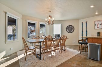 The dining area at Blue Bird on Norfolk featuring a wooden dining table and chairs, illuminated by natural light and a chandelier, with a view of a winter landscape outside.