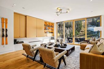 A luxurious living room in Founders Place 2502 with modern furniture, a large window revealing a snowy forest, and ski decor.